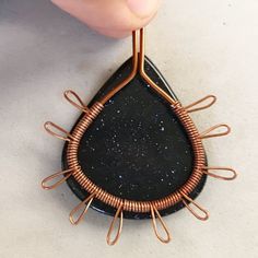 a person holding a wire wrapped pendant with black stone and copper colored wires attached to it