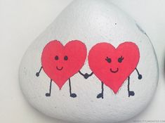 two red hearts holding hands on top of a white rock next to a black clock