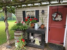 an outdoor garden with potted plants and flowers on the side of a house next to a red door