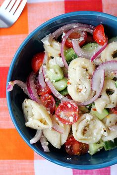 a blue bowl filled with pasta salad on top of a checkered table cloth next to a fork