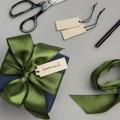 a green bow and some scissors on a gray table with name tags attached to it