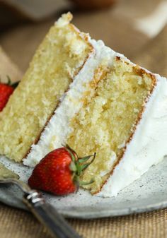 a slice of cake with white frosting and strawberries on the plate next to it