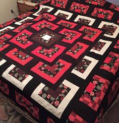 a bed with a black and pink quilt on it's cover, next to a night stand