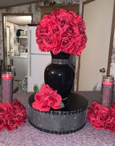 a black vase with red roses in it sitting on a table next to other items