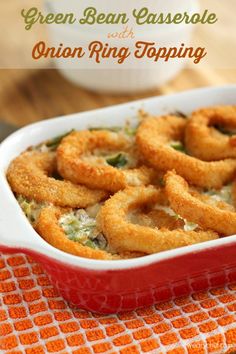 green bean casserole with onion ring topping in a red dish on an orange and white towel