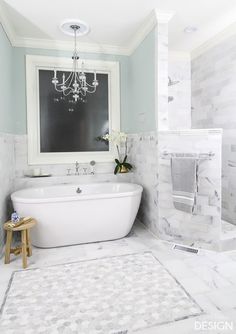 a white bath tub sitting in a bathroom next to a sink and mirror with a chandelier hanging above it