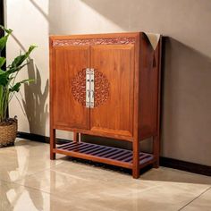 a wooden cabinet sitting next to a potted plant on top of a tiled floor