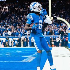 a football player is running on the field with his hand up to his face as he celebrates