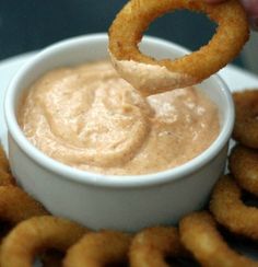 a person dipping some onion rings into a small white bowl filled with mayonnaise