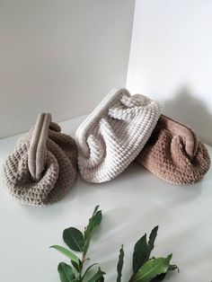 three crocheted bags sitting on top of a white table next to green leaves