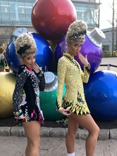 two women dressed in costumes standing next to each other near large balls on the ground