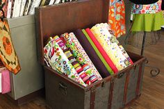 an old trunk filled with lots of colorful fabrics and quilting material on top of a hard wood floor