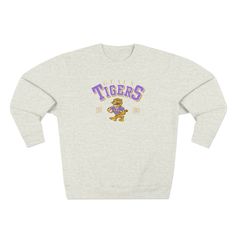 Gear up for chilly game days and tailgating with this stylish LSU Geaux Tigers Sweatshirt! Featuring a retro tiger design, it's the perfect blend of comfort and fashion for dedicated fans. This cute women's game day apparel is a must-have for every LSU supporter looking to showcase their team spirit. Shop now to ensure you stay warm and trendy while cheering on the Tigers this season! Featuring a 3-end fleece fabric, it has a real tight-knit construction giving it better quality and durability. It's not only beautiful but also comfy and soft to the touch with the best in its class and under 5% shrinkage. *Key Features* .: 80% cotton, 20% polyester  .: Medium-heavy fabric (8.25 oz /yd² (280 g/m .: Regular fit .: Tear away label .: Runs true to size Lsu Sweatshirt, Lsu Baseball, Cute Game, Football Top, Lsu Football, Geaux Tigers, Football Tops, Sweatshirt Trendy, Tiger Design