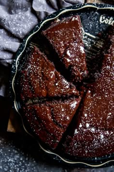 a chocolate cake with powdered sugar on top sits in a black bowl next to some napkins