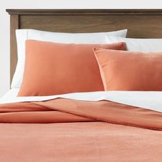 a bed with an orange comforter and two pillow cases on top of the headboard