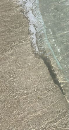 a person walking on the beach with a surfboard in their hand and an ocean wave coming toward them