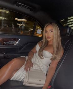 a woman sitting in the back seat of a car wearing a white dress and heels