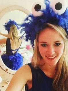 a young woman is smiling in front of a mirror wearing a blue fuzzy monster hat