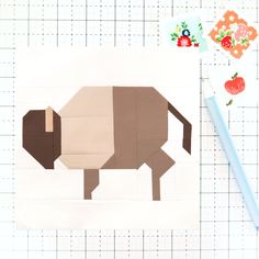 an animal made out of paper sitting on top of a cutting mat next to a pencil