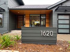 the address sign is displayed in front of a house with wood siding and large windows