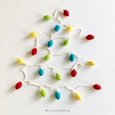 crocheted christmas lights hanging from strings on white tablecloth with red, green and blue balls