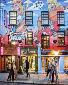 people walking down the sidewalk in front of a tattoo shop with an advertisement painted on it