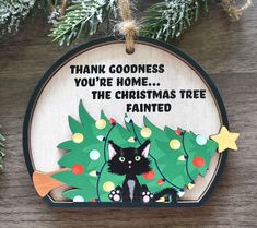 a christmas ornament with a black cat on it's back and the words thank goodness you're home, the christmas tree is painted