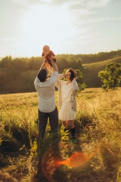 a man and woman holding up a baby in a field with the sun behind them