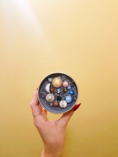 a hand holding a small bowl filled with different types of marbles on top of a yellow background