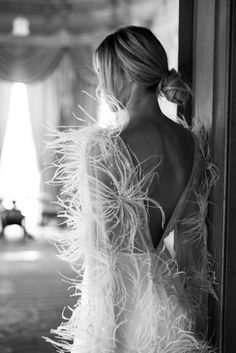 a woman in a feathered dress leaning against a wall with her back to the camera