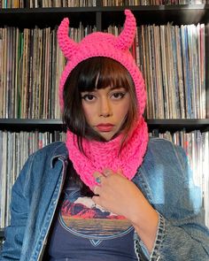 a woman wearing a pink knitted cat hat and scarf in front of a bookshelf