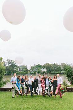 a group of people standing on top of a lush green field next to a lake