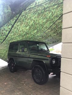 a green suv parked under a camouflage covered tent