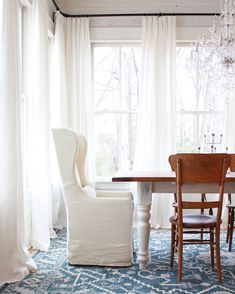 the dining room table and chairs are in front of an open window with white curtains