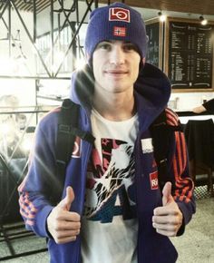 a man wearing a blue hat and jacket giving the thumbs up while standing in an airport