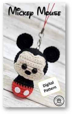 a crocheted mickey mouse keychain hanging from a string on a white wooden background