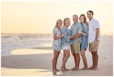 a group of people standing on top of a beach next to the ocean at sunset