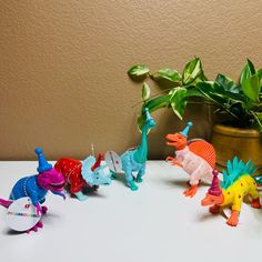 small toy dinosaurs lined up on a table next to a potted plant