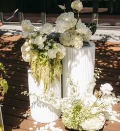 two white vases filled with flowers sitting on top of a wooden floor next to each other