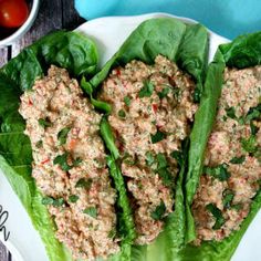 two lettuce wraps filled with meat on top of a white plate next to tomatoes