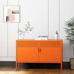 an orange cabinet in a white room next to a potted plant