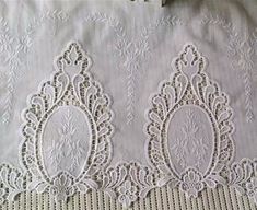 two white laces are sitting on top of a tablecloth with an embroidered design