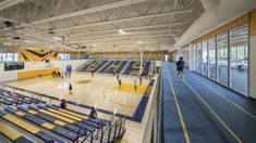 an indoor basketball court with blue and yellow seats, people playing basketball on the floor