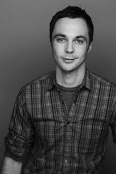 a man wearing a red and black checkered shirt is smiling at the camera while standing in front of a gray wall