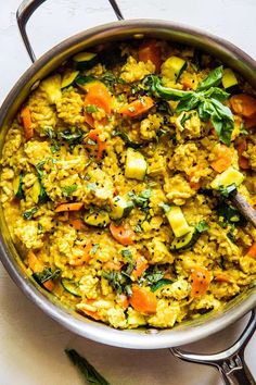 a pot filled with rice and vegetables on top of a white counter next to a wooden spoon