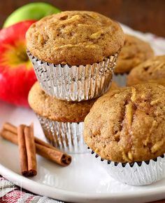 three muffins on a plate with cinnamon sticks and an apple in the background