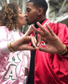 a man and woman standing next to each other making the peace sign with their hands