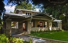 a house with green grass and trees in the front yard, along with a walkway leading up to it