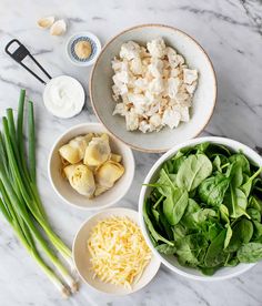 the ingredients for this salad are laid out in bowls on the marble counter top, including onions, celery, cheese and spinach