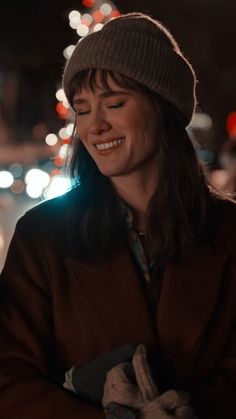 a woman smiles as she holds her hands together in front of a city street at night